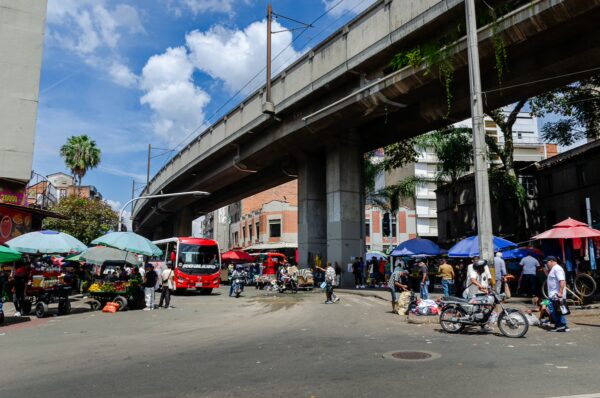 Street vendors and colorful umbrellas gather beneath a metro line in Medellín, Antioquia, showcasing vibrant local life.
