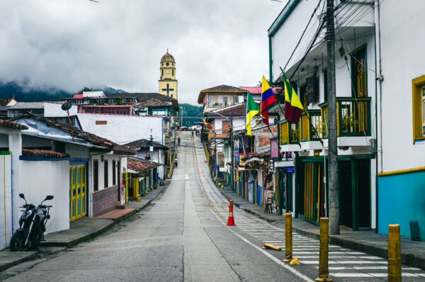 Colorful houses line a quiet street in Salento, Quindío, with a backdrop of a church tower and flags fluttering in the breeze.