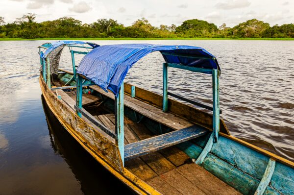 Weathered boat with a blue canopy on the serene waters of Pirana Lake, surrounded by lush greenery in Gamboa Nature Reserve, Loreto, Peru.