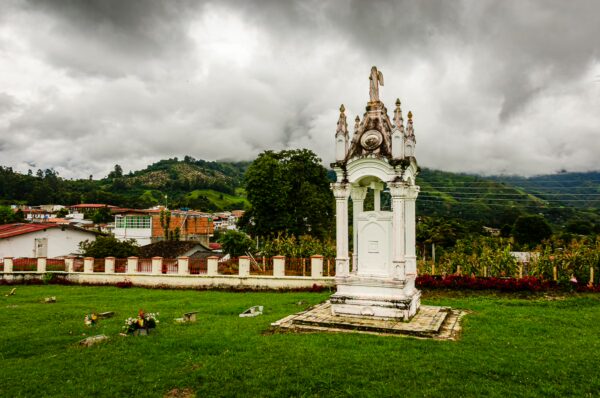 White mausoleum stands in a green field with a backdrop of rolling hills and cloudy skies in Salento, Quindio, Colombia.