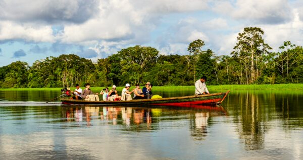 Piranha Lake shows a colorful boat with several passengers gliding through calm waters, surrounded by lush greenery in Gamboa Nature Reserve, Loreto, Peru.
