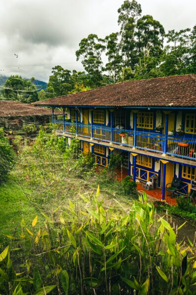 Colorful colonial-style buildings surrounded by lush greenery in Salento, Quindío, Colombia, showcasing vibrant blue and yellow hues.