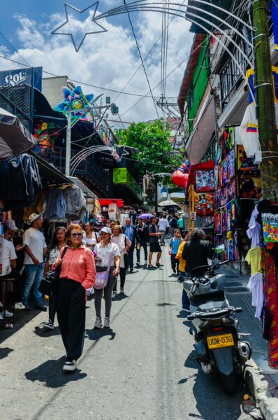 Vibrant street scene in Comuna 13, Medellín, featuring colorful market stalls and people strolling under a bright blue sky.