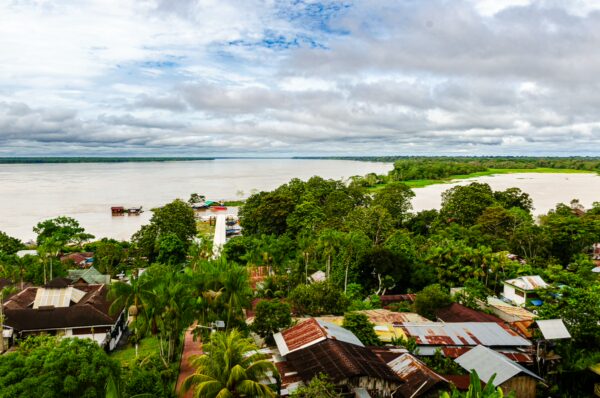 Lush green trees and colorful rooftops contrast with the tranquil waters of the Amazon River in Puerto Narino, Colombia.
