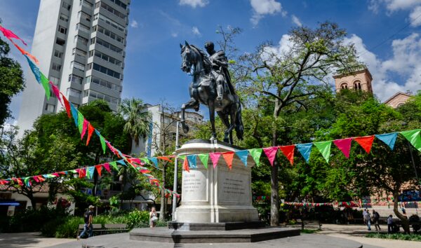 Simón Bolívar statue in Parque de Bolívar with trees, bunting, and city buildings in Medellín