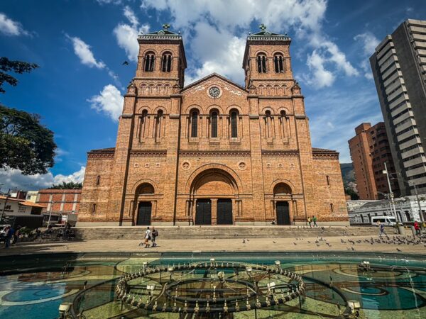 Metropolitan Cathedral of Medellín with twin brick towers overlooking a plaza and fountain under a blue sky