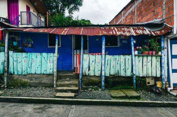 Colorful blue house with a corrugated roof and vibrant flowers in pots, set in Salento, Quindío, Colombia.