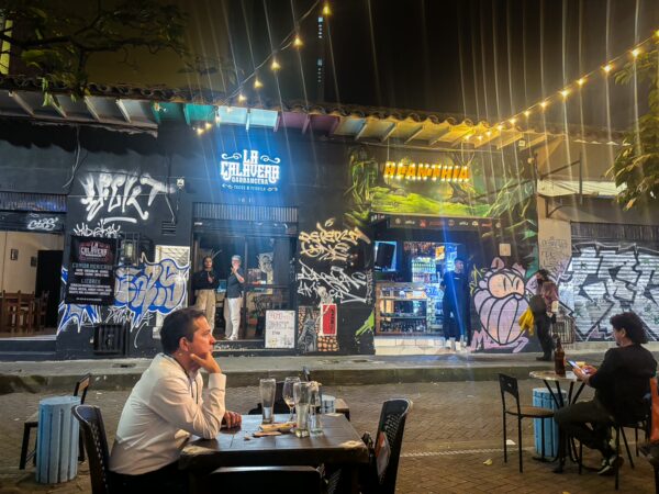 Vibrant street scene at Carrera 42A in Medellín, showcasing colorful graffiti and lively outdoor dining under string lights.