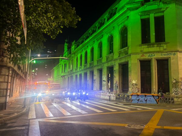 A vibrant street scene in Medellín, illuminated by green lights from historic buildings, with cars and street markings adding urban charm.