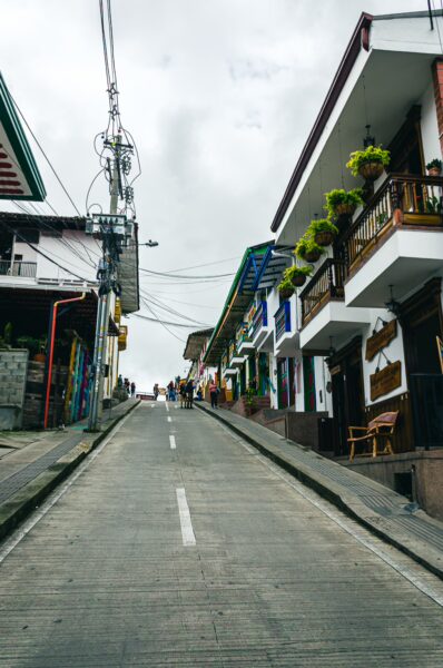 Charming hillside street in Salento, Quindio, Colombia, featuring colorful houses and vibrant green plants, set against a cloudy sky.