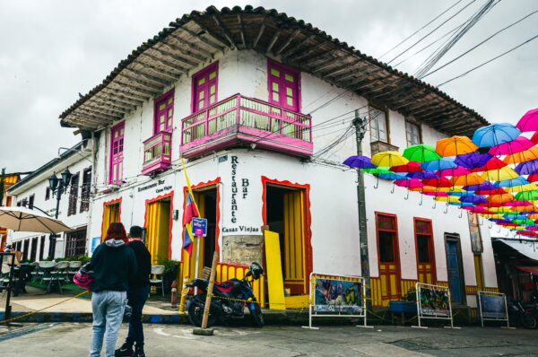 Colorful umbrellas hang above a vibrant building in Celle Real, Salento, showcasing the charm of Quindio, Colombia.