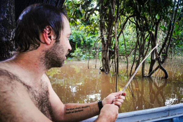 A man sitting in a boat, fishing among lush greenery and murky waters at Gamboa Nature Reserve, Loreto, Peru.