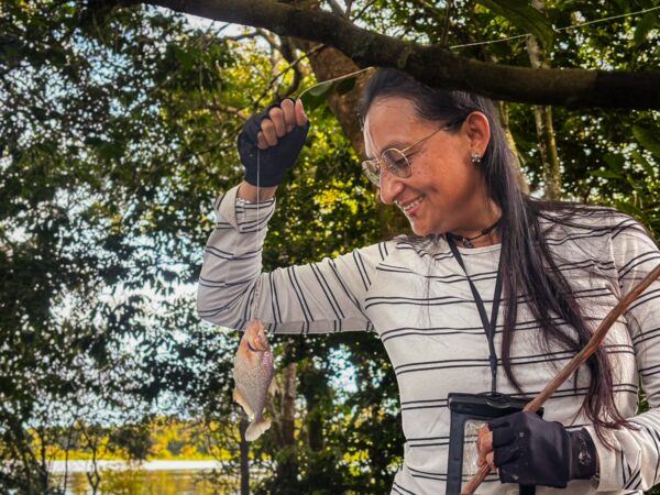 A woman in a striped shirt holds a freshly caught fish amid lush greenery at Gamboa Nature Reserve in Loreto, Peru.