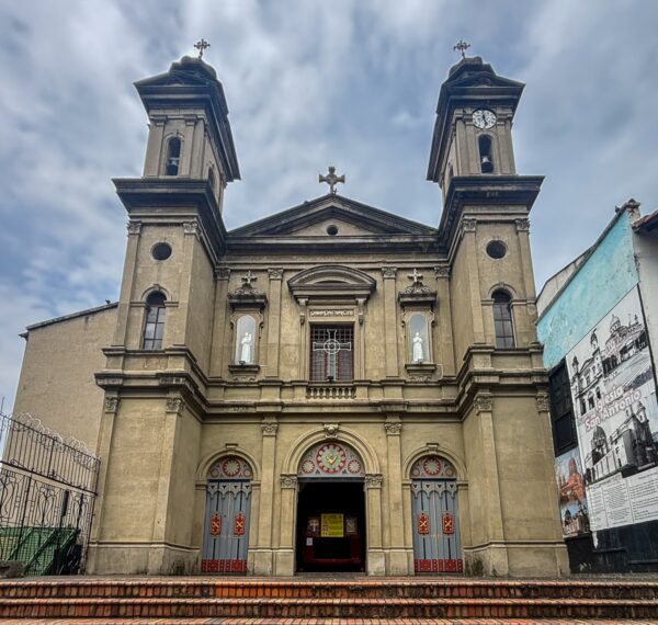San Antonio Church in central Medellín, with a symmetrical façade and twin bell towers against a cloudy sky