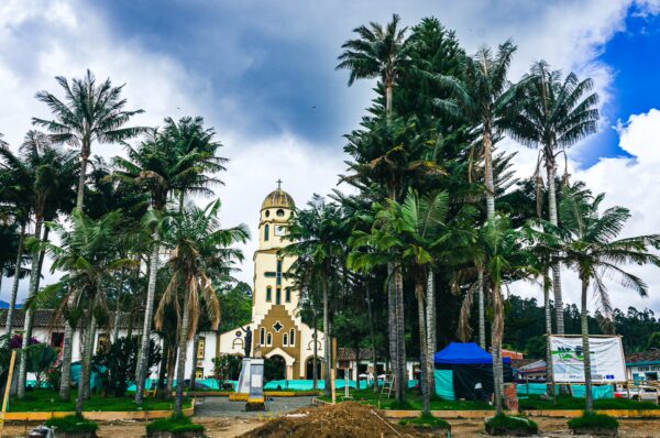 Coconut palms surround a charming church in Plaza Bolívar, showcasing the vibrant scenery of Salento, Quindío, Colombia.