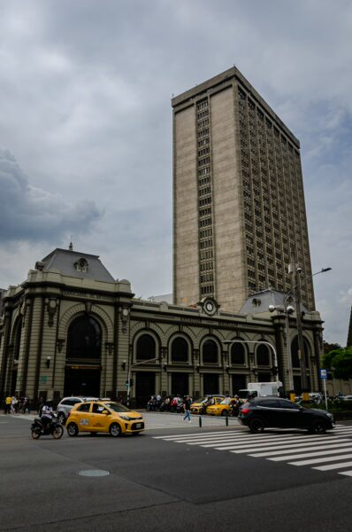 Historic architecture and modern skyscraper contrast at Parque de las Luces in Medellín, with yellow taxis bustling through traffic.