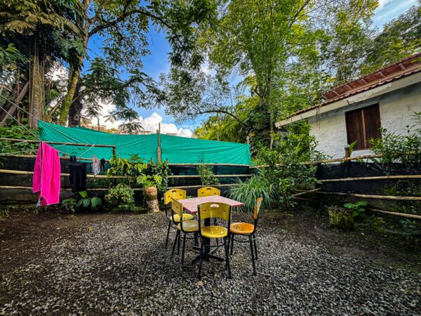 Colorful chairs surround a table in a lush garden, featuring vibrant greenery and a blue sky in Velez, Salento, Quindio, Colombia.