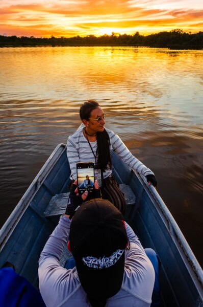 Sunset reflections on the water as two travelers capture the scene in a boat at Gamboa Nature Reserve, Loreto, Peru.
