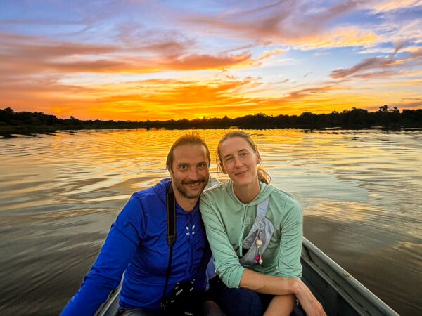 Caiman spotted at Lake Gamboa during a vibrant sunset in Loreto, Peru, with two travelers enjoying the serene landscape.