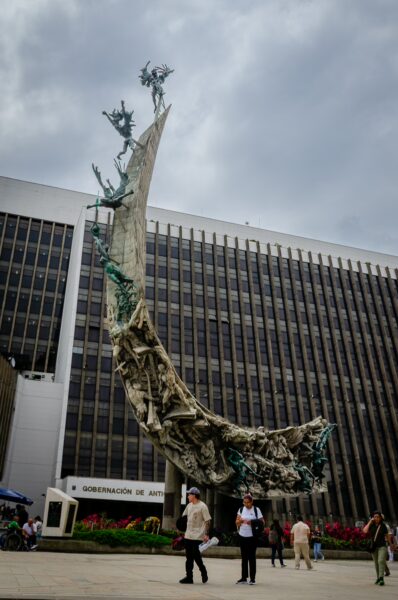 Monumento a la Raza in Medellín features an artistic sculpture set against a modern building backdrop on a cloudy day.