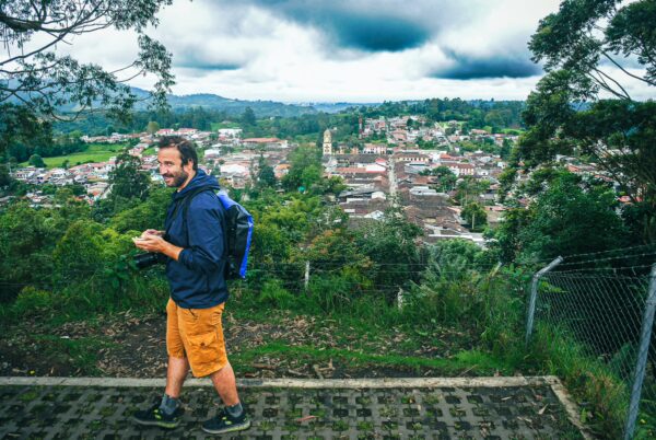 A traveler enjoys a scenic view of Salento, Colombia, with rolling green hills and the town's colorful rooftops visible below.
