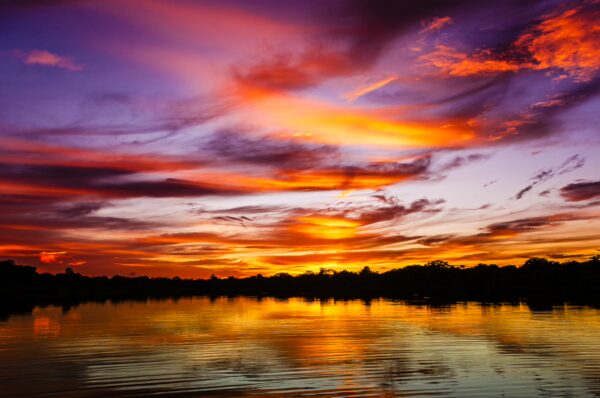 Vibrant sunset reflected on calm waters in Gamboa Nature Reserve, highlighting rich purple and orange hues over the landscape.