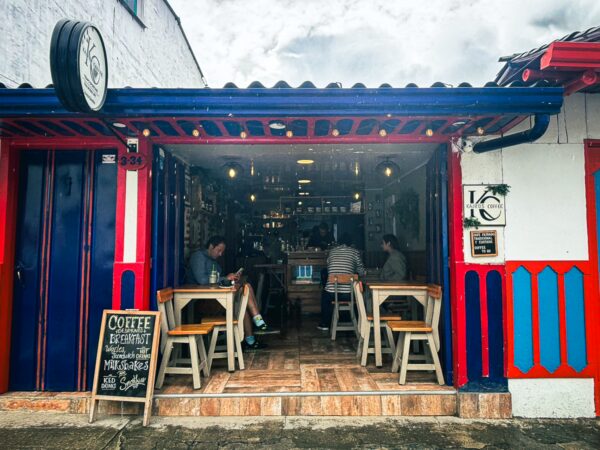 Kairos Coffee in Salento features vibrant red and blue decor, inviting outdoor seating, and patrons enjoying their drinks in Quindío, Colombia.