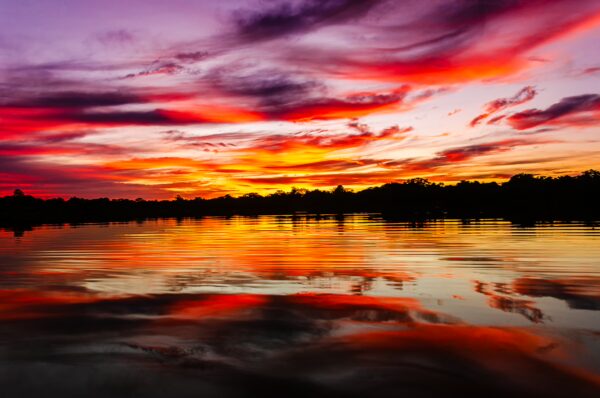 Vibrant sunset hues reflect on the calm waters of Gamboa Nature Reserve, showcasing the rich colors of Loreto, Peru.