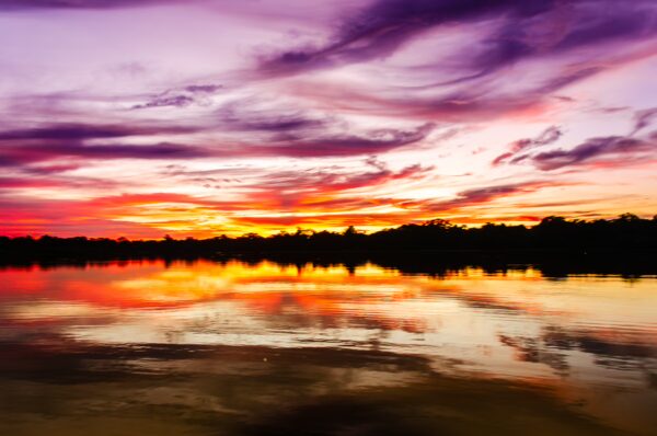 Vibrant sunset colors reflect on calm waters at Caiman Lake in Gamboa Nature Reserve, Loreto, Peru.