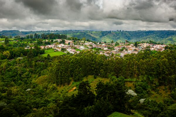 Lush green hills surround the colorful town of Salento in Quindío, Colombia, set against a dramatic cloudy sky.
