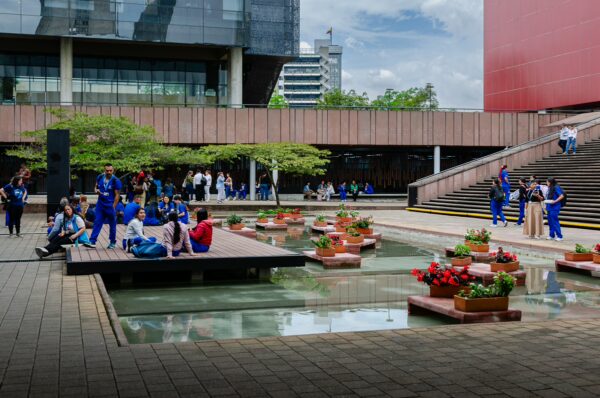 Plaza de La Libertad in Medellín, with modern civic buildings, a reflecting pool, flower planters, and people sitting on steps and platforms