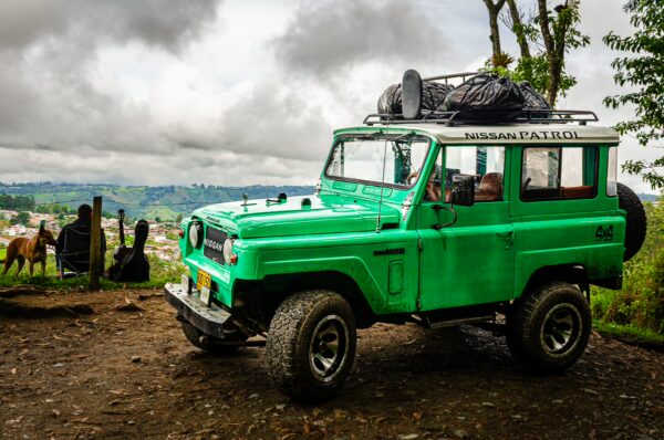 Bright green safari vehicle parked at Mirador de la Valle in Salento, Quindio, with lush hills and cloudy skies in the background.