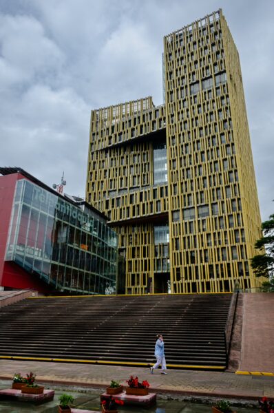 Modern civic building in Medellín with a tall slatted tower, red glass volume, and wide steps in front