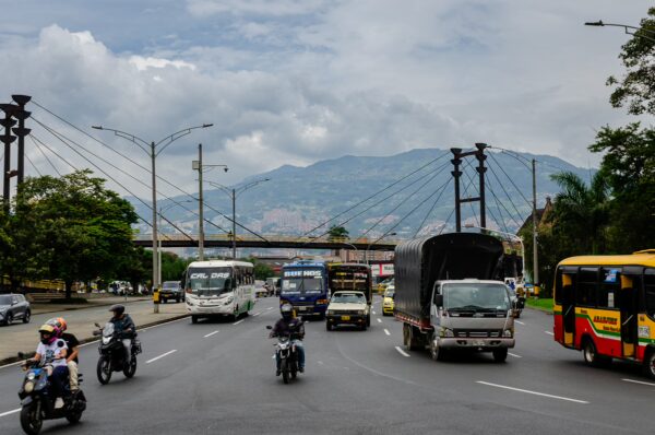 Busy Medellín roadway with buses, motorcycles, and mountain views in the background