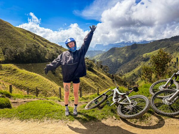 Biker posing joyfully on a hillside in Carbonera Valley, Quindío, Colombia, with green mountains and bicycles nearby.