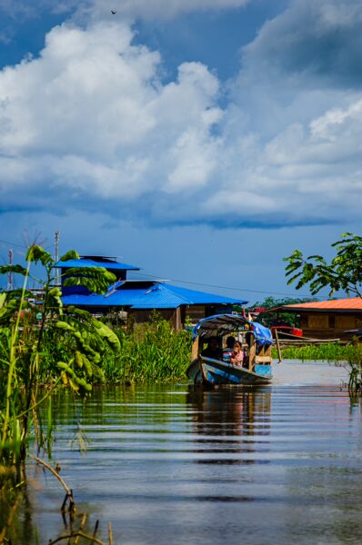 Colorful boats navigate the calm waters surrounded by lush greenery and blue-roofed buildings in Santa Rosa, Amazonas, Peru.