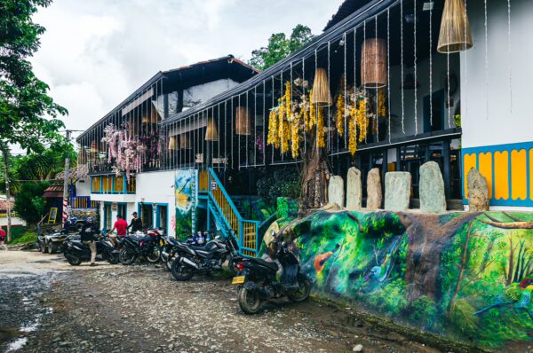 Colorful buildings adorned with hanging decorations and vibrant murals, nestled in Salento, Quindío, Colombia, with parked motorcycles.