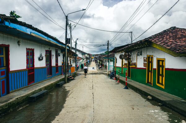 Colorful houses line Calle Real in Salento, Quindio, Colombia, under a cloudy sky, showcasing vibrant doors and lovely street details.