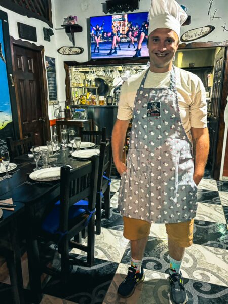 Enjoying a cooking class in Salento, a chef in a polka-dotted apron stands in a cozy restaurant with colorful decor.
