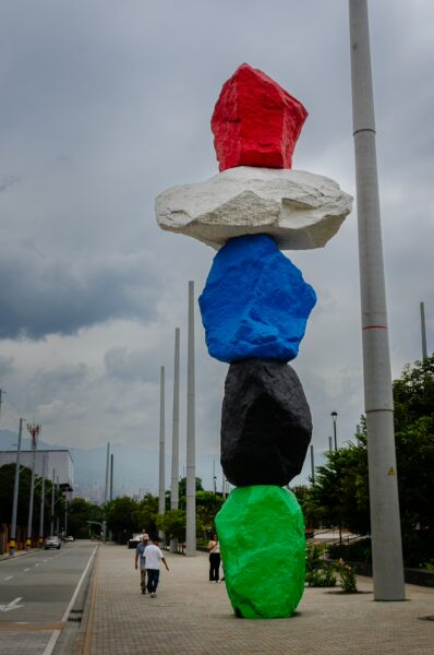 Vibrant colorful rock sculptures tower over a pathway in Parque Río Etapa, Medellín, set against a cloudy sky.