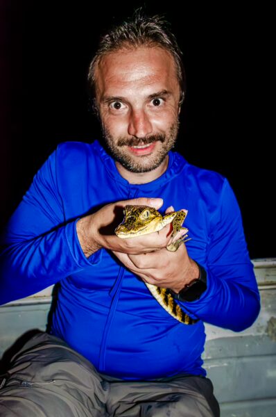 A man in a blue shirt holds a caiman in the Gamboa Nature Reserve, showcasing the rich wildlife of Loreto, Peru.