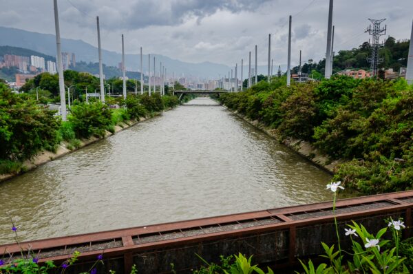Medellín River channel with bridges, green riverbanks, and the city and mountains in the distance