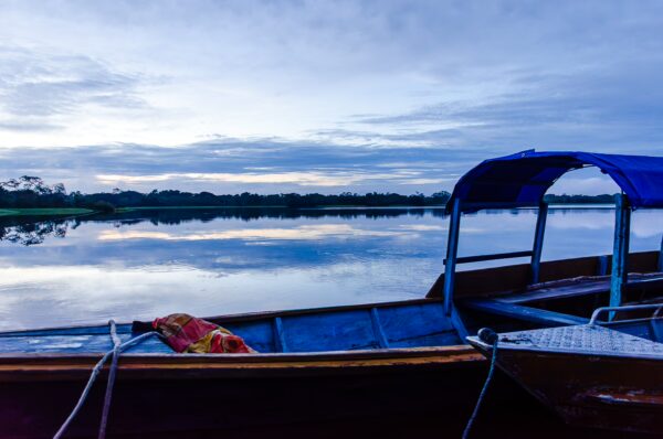 Piranha Lake at Gamboa Nature Reserve features calm waters reflecting the twilight sky, with wooden boats lined by the shore in Loreto, Peru.