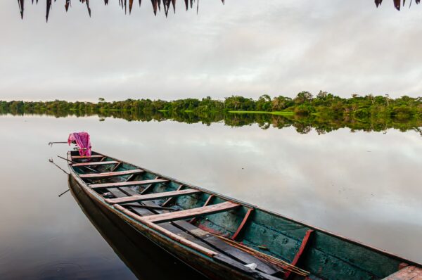 Piranha Lake reflects lush greenery and a tranquil sky, with a canoe resting peacefully at the edge in Gamboa Nature Reserve, Loreto, Peru.
