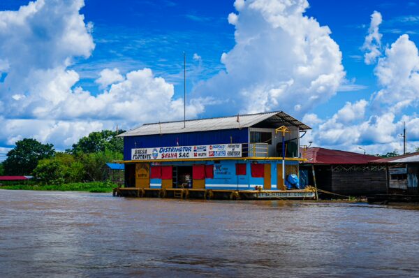 Brightly painted houses line the riverbank, reflecting on the waters of Santa Rosa, Amazonas, Peru, under a vibrant blue sky.