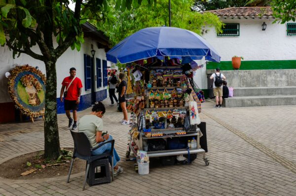 Colorful craft stand at Pueblito Paisa in Medellín, surrounded by visitors and green trees, showcasing local artisan goods.