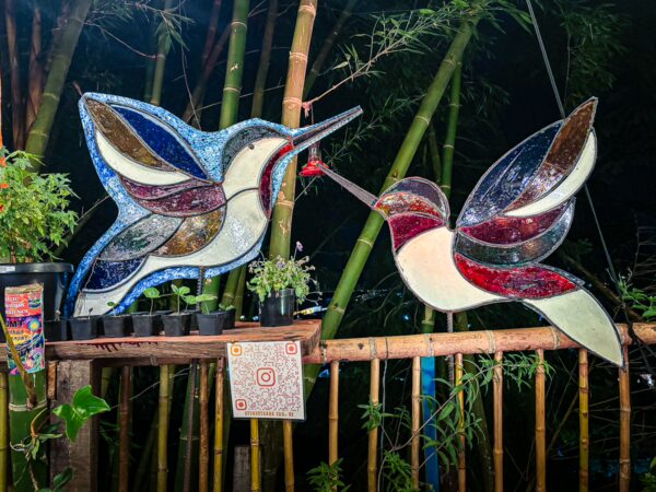 Colorful mosaic hummingbirds vibrantly decorate a wooden display amidst lush green bamboo in Salento, Quindio, Colombia.