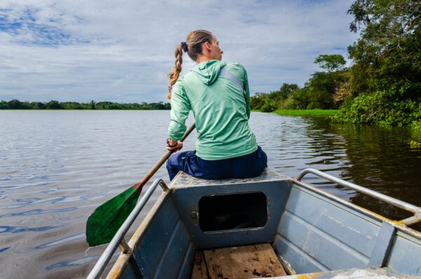 Paddling a boat on Pirana Lake, surrounded by lush greenery in Gamboa Nature Reserve, Loreto, Peru. Clear skies reflect on the water.