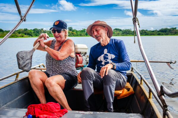 Two tourists enjoy a boat ride on Pirana Lake in Gamboa Nature Reserve, surrounded by lush greenery under a bright blue sky.