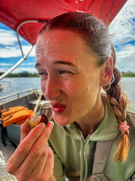 Enjoying a camu camu fruit on a boat in Gamboa Nature Reserve, surrounded by lush greenery and a bright blue sky in Loreto, Peru.